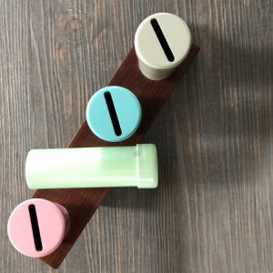 Vier bunte, zylindrische Münzsammler auf Holzständer, geeignet für Sparziele oder Organisation, in Pastelltönen.