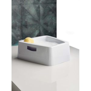 Fußbadewanne mit Schaum und Schwamm auf weißer Oberfläche vor grauer Wand, ideal für entspannende Fußpflege.